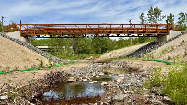 A pedestrian bridge spans a creek lined with supportive construction materials