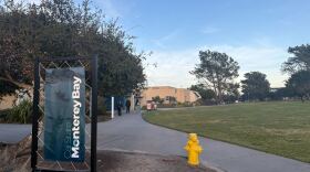 A vertical banner that reads Cal State Monterey Bay stands next to a walking path with a yellow fire hydrant beside it.