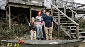 Ollie and Daniel Williams stand in front of their raised home with their children Trinity, 9, and Masen, 12. The land surrounding their house floods so often that the family keeps a small fiberglass canoe tied to the bottom of the front steps and a flat-bottom boat tied to the side of their house to aid in evacuating.