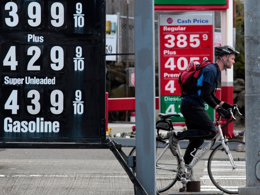 A bicyclist waits at an intersection between competing gas stations and multiple posted gas prices on Monday in Seattle.
