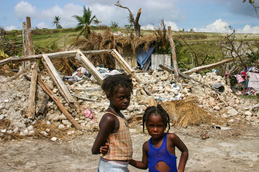 Girls stand in front of their destroyed home in the Dumont section of Port Salut, Haiti. They're now living in the thatched shack that's directly behind the rubble of their home.