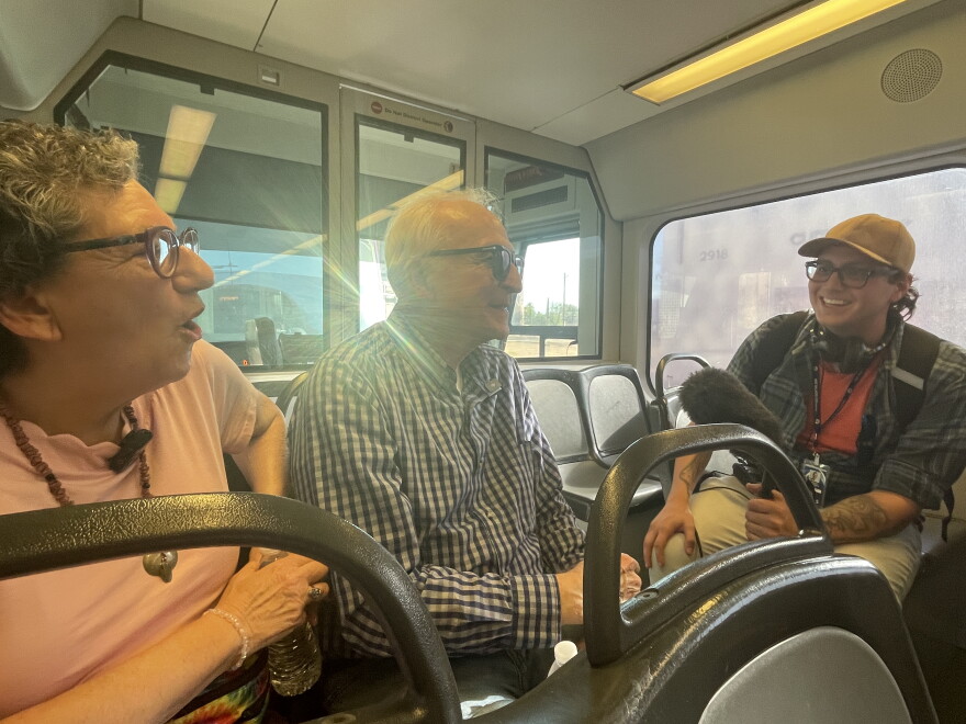 Two people sit in light rail seat with another person across
