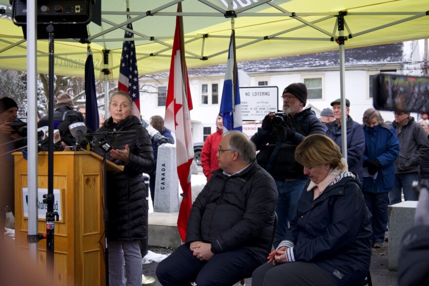 A woman stands at a podium under a tent to speak