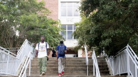  Two students walk down a long staircase. In back of them is a brick, campus building