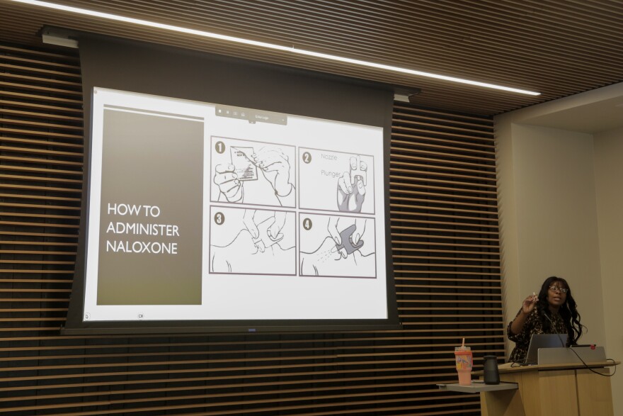 Ariea Alexander gives a presentation on how to administer Naloxone, the screen behind her shows four steps for using the nasal spray.