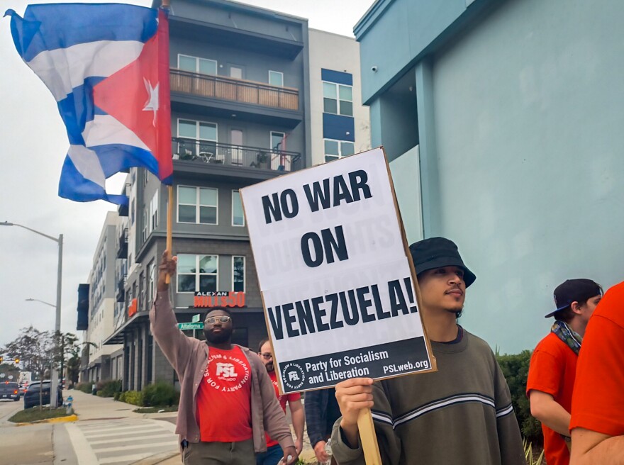 Ramón Pereira Bonilla (right) marches through Mills 50 on Saturday, carrying a sign urging against U.S. military intervention in Venezuela.