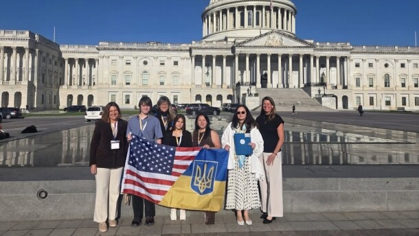 Seven people stand in front of the U.S. Capitol. They are holding a joint U.S./Ukrainian flag.