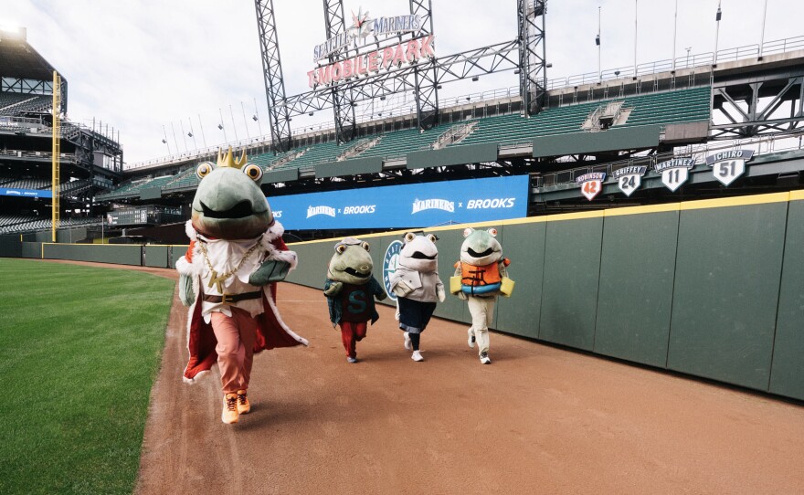 Four people dressed in salmon costumes run on a baseball field