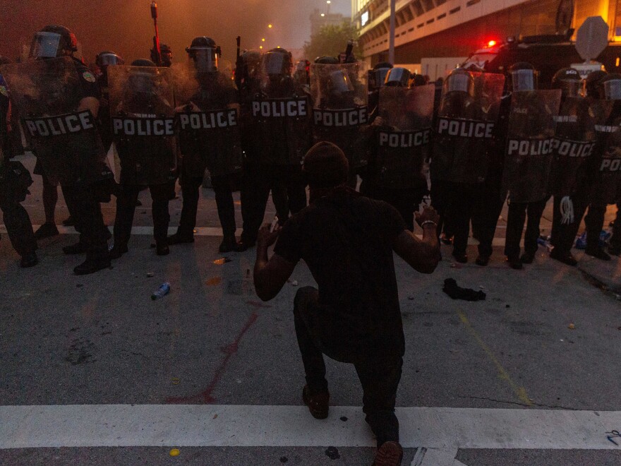 A protestor kneels and raises his hand in front of a line of riot police during a protest against police brutality in Miami on May 30, in response to the recent death of George Floyd, an unarmed black man who was killed by police.