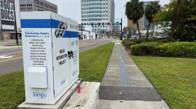 Solar Sidewalk in Downtown Tampa, which is raised compared to the rest of the sidewalk, with some metal paneling on top of it, along an intersection with some buildings in the backdrop.