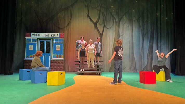 People standing on a green and yellow stage with red, blue and yellow blocks around the floor.