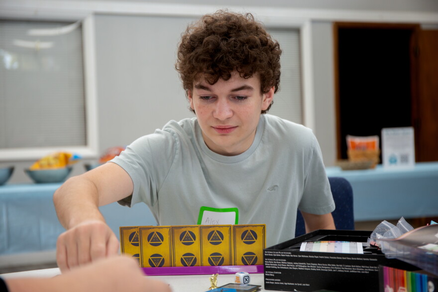 A teenage boy with short, curly brown hair sets up a boardgame that is mostly cards and little plastic tokens. 