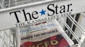 A newspaper sits flat in a wire rack inside a grocery store. The metal rack has a label that reads: "The Star."