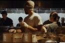 Several people stand in a food prep room, wearing hats and gloves. They are assembling free meals for a Thanksgiving event.