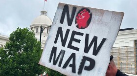 A demonstrator holds up a sign outside the Alabama Statehouse in Montgomery, Ala., on Thursday, May, 7 2026. (AP Photo/Kim Chandler)