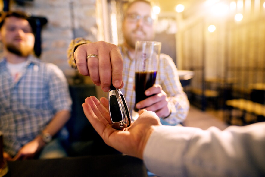 Drunk man with a beer in hand giving car key to the sober friend while enjoying in the bar.