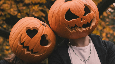 Two people with pumpkins on their heads with pumpkin carvings in a smile