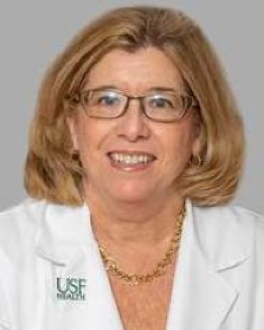 Dr. Patricia Emmanuel wears a lab coat and glasses and smiles for camera in professional headshot