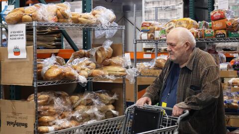 Richard Beveo pushes a shopping cart through the Cache Community Food Pantry. Behind him are shelves stocked with bread. 