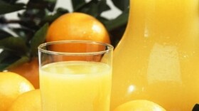 Orange juice in a glass with whole oranges in the background