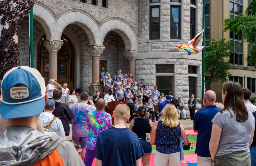 LGBTQ+ community members in Syracuse watch speaker, Jaleel Campbell, as the Pride Flag waves in front of city hall.