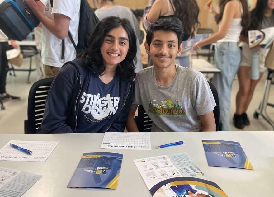 Tayba and Abraham Khan sit at a desk, posing for a photo.