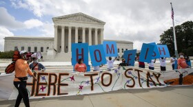 Banners in from of the Supreme Court building say "Homeish" and "Here to stay." There are people with masks holding up the signs.