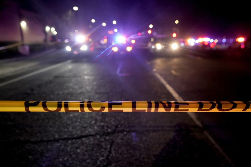 Police tape across a road at night. Police cars with lights on in the background.