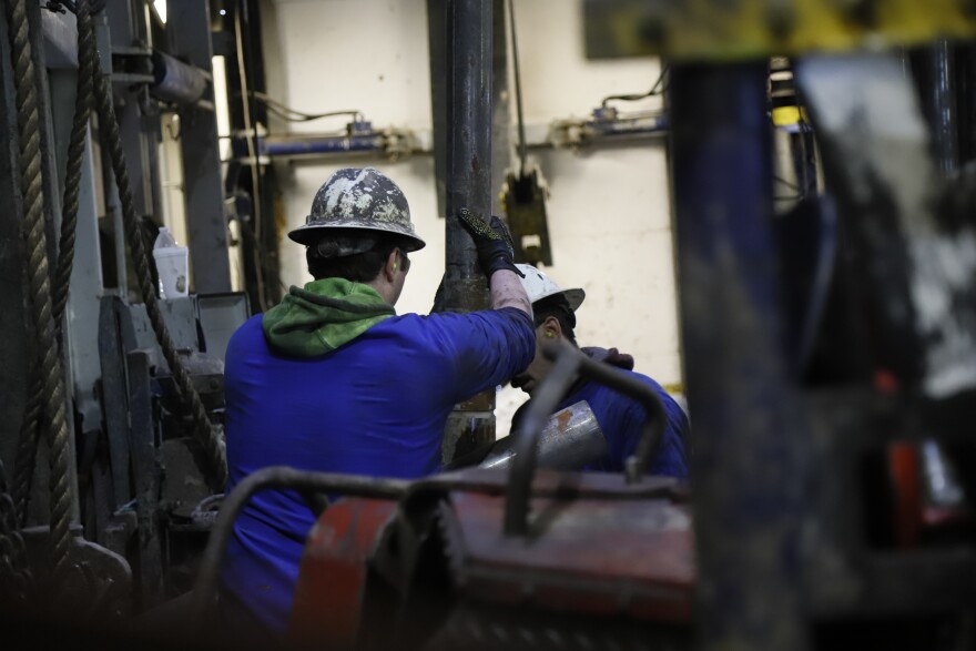 Two Santos employees work with drill pipe at the Pikka drill rig site.
