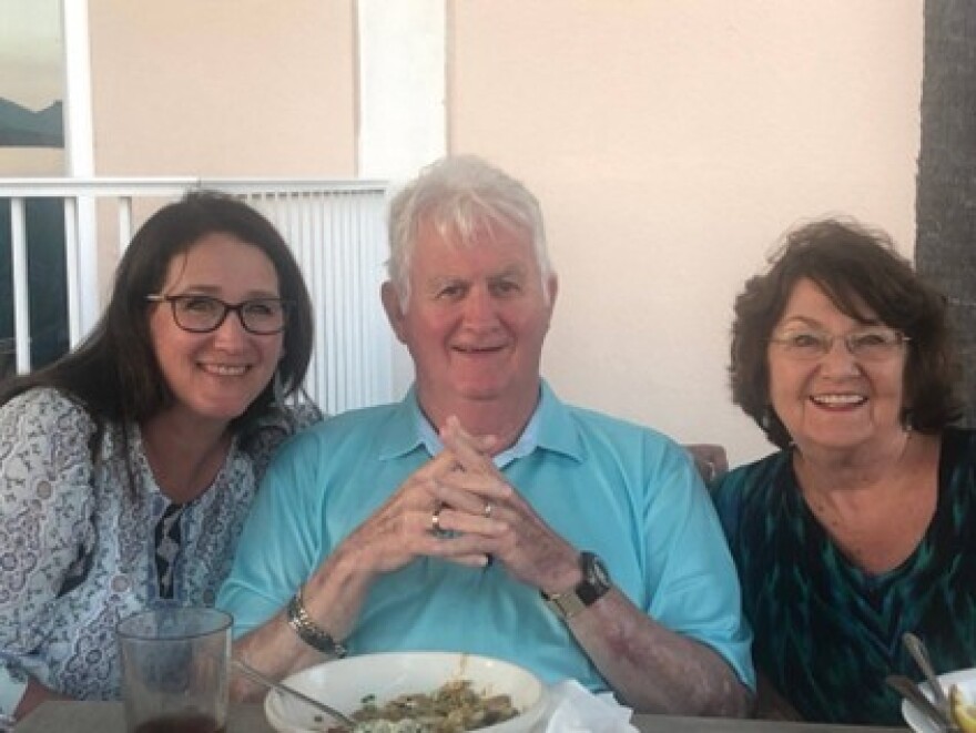 Two women seated beside a man with his hands clasped, pose for a photo.