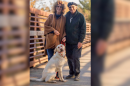 A couple standing on a bridge with a white dog in front of them.