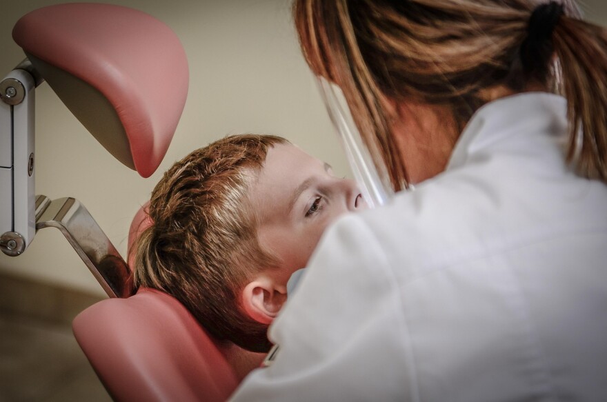 A boy is examined while sitting in a dentist's chair.