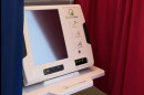 Electronic voting machine with a blank screen surrounded by a blue curtain on the left and a red curtain on the right. 