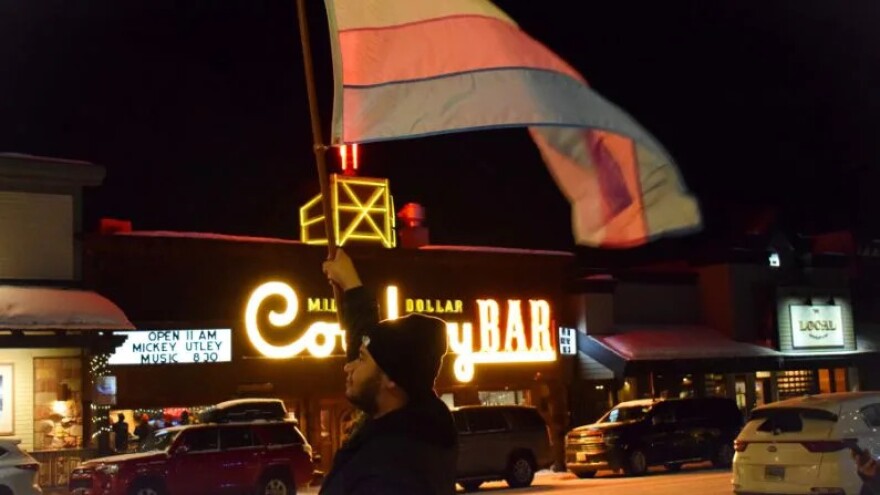  Jackson resident Mars William Silva waves a pink and blue flag — the transgender colors — in front of the Cowboy Bar near town square on Feb. 27, during a vigil for Nex Benedict, a nonbinary teenager who recently died in Oklahoma.&nbsp;