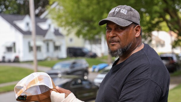 Hipolito Mateo stands in the front yard of his Rochester home Monday, May 18, 2026, holding the hat he said was marked with orange spray residue after ICE agents pepper-sprayed him during an encounter on Northland Avenue. Mateo said he was tased by the agents and fractured his wrist in a fall after agents blocked in his and his workers’ vehicles while they were preparing to begin the workday.
