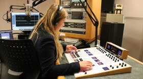 Young woman wearing headphones works on a radio mixing board.