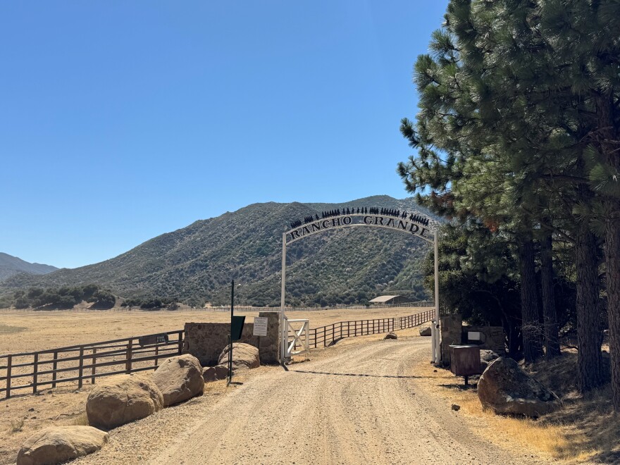 An overhead gate marks a ranch boundary. The gate is over a dirt road. The signage on the gate reads 'Rancho Grande.'