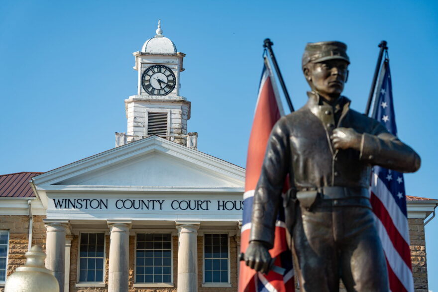 A statue of a Civil War-era soldier, with Confederate and American flags behind it, stands in front of the Winston County Court House.