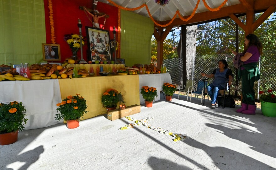 Shadows of woman sitting at the ofrenda are cast on the floor.