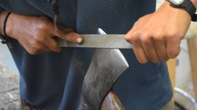 A person sharpens the blade of a hatchet
