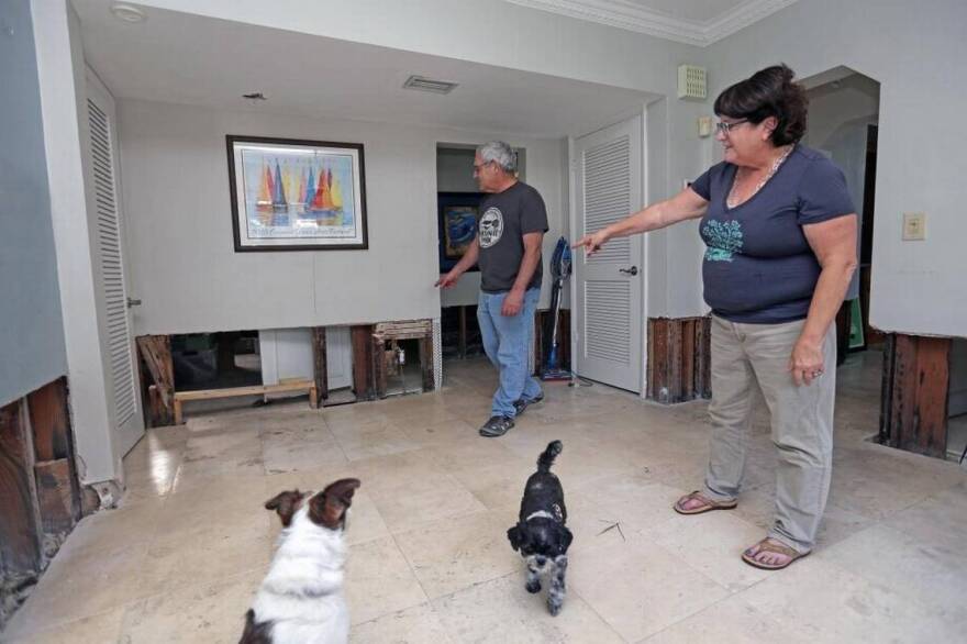 Couple standing in their house pointing to a lower portion of walls that were removed due to floodwaters