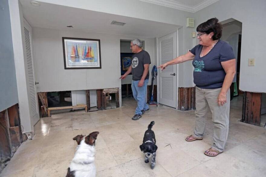 Couple standing in their house pointing to a  lower portion of walls that were removed due to floodwaters 