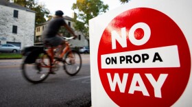 A biker passes a "No on Prop A Way" sign. 