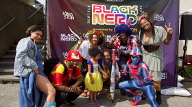 People in colorful costumes pose in front of a banner.