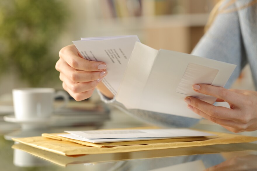 A woman's hands open up an envelope while sitting at a glass table.