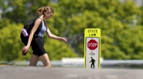 woman walking with a backpack past a pedestrian crossing sign