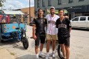 Three men pose for a photo in front of a pedicab on the street.