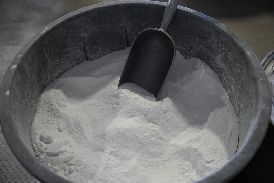The viewer is looking down into a grey container filled with white powder. A grey scoop is lightly dug in.