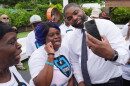 Black man in white dressshirt and tie  leans over to take a smartphone selfie with a shorter black woman in a white tshirt