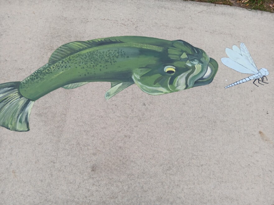 A painting of a fish and a dragonfly on a sidewalk.